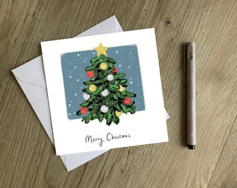 Può includere: Un biglietto di Natale con un albero di Natale verde decorato con palline rosse, gialle e bianche. L'albero ha una stella dorata in cima ed è su uno sfondo blu con fiocchi di neve bianchi. Il biglietto dice "Buon Natale".