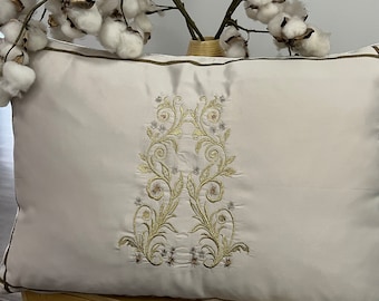 May include: A white pillow with a brown border and a gold embroidered floral design.