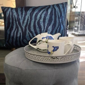 May include: A gray ottoman with a blue and black zebra patterned pillow, a white teapot with blue floral designs, and two white mugs with blue floral designs on a gray metal tray.