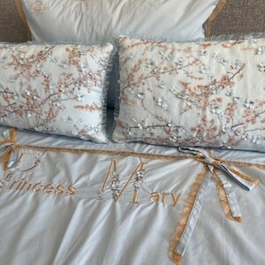 May include: A light blue bedding set with two floral patterned pillowcases. The bedding has the words "Princess Mary" embroidered on it.