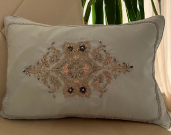 May include: A light blue throw pillow with a decorative embroidered design featuring gold and silver sequins and beads.
