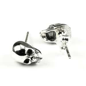 May include: A pair of silver skull stud earrings. The earrings are made of metal and feature a detailed skull design.