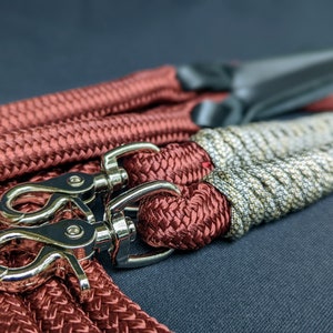 May include: Two dog leashes with silver clips. One leash is red and the other is a combination of gray and brown.