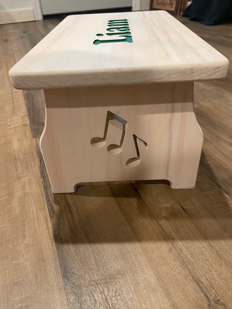 Left side of a white stained single step children's step stool with music notes cut into the side with a CNC machine.