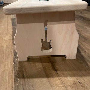 Image of the right side of a stained white single step stool with a guitar cut into the side made by a CNC machine.