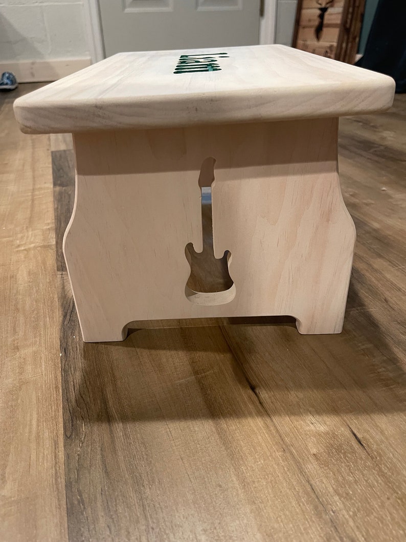 Image of the right side of a stained white single step stool with a guitar cut into the side made by a CNC machine.