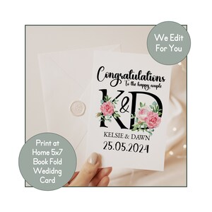 May include: A white wedding card with black calligraphy that reads "Congratulations to the happy couple" and "K&D" with floral accents. The names "Kelsie & Dawn" and the date "25.05.2024" are printed below the floral initials.