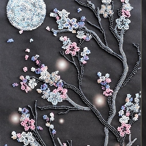 May include: A beaded artwork depicting a night scene with a full moon and flowering branches. The moon is a cluster of white and blue beads. The branches are black with clusters of pink, white, and blue beaded flowers. The background is dark.