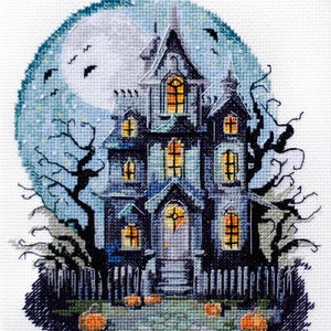 May include: A cross-stitch pattern of a spooky, blue and gray haunted house with glowing windows, a full moon, bats, and pumpkins in front of a white picket fence.