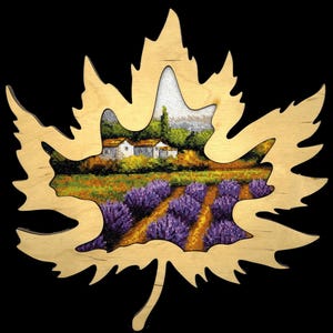 Peut inclure: Une découpe en bois en forme de feuille d'érable avec une image au point de croix d'un champ de lavande et d'un petit village en arrière-plan.