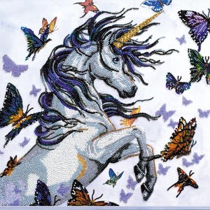 May include: A detailed beaded artwork of a white unicorn with a golden horn and flowing dark blue and purple mane. Colourful butterflies in shades of orange, blue, and purple surround the unicorn, creating a whimsical scene.