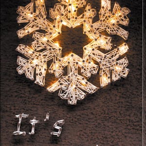 May include: A decorative snowflake made of white string and small lights, illuminated against a dark background. The words "It's snowing" are spelled out below the snowflake using the same material. A festive winter decoration.