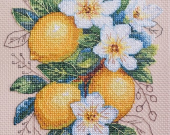 Puede incluir: Bordado de punto de cruz de limones y flores blancas con hojas verdes sobre un fondo marrón claro.