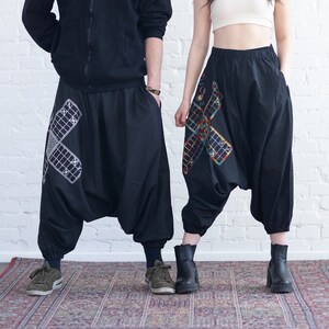 Könnte beinhalten: Zwei Personen tragen schwarze Hosen mit bunten Stickereien. Die Hosen sind weit geschnitten und haben eine weite Beinweite. Die Personen stehen auf einem gemusterten Teppich vor einer weißen Backsteinwand.