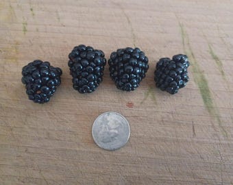 May include: Four ripe blackberries with a quarter coin for size comparison, arranged on a wooden surface. The blackberries are a deep, glossy black, showcasing their characteristic bumpy texture. The quarter provides a sense of scale.