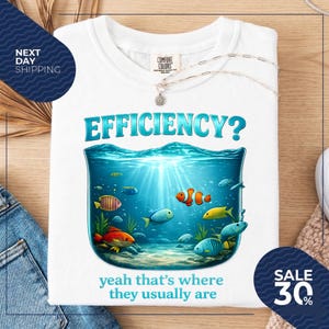 May include: A white t-shirt featuring a graphic of an underwater scene inside a glass container. The text EFFICIENCY? appears above the water, and the text yeah that's where they usually are appears below. Various colourful fish swim inside.