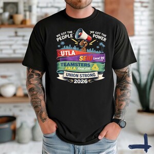 May include: Black t-shirt with a graphic design featuring the text "WE GOT THE PEOPLE" and "WE GOT THE POWER". The design includes a megaphone, city skyline, and the words "UTLA", "SEIU", "Teamsters", and "Union Strong 2026".