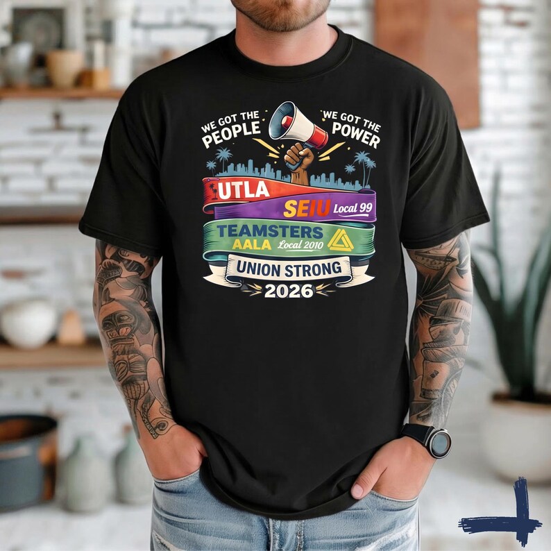 May include: Black t-shirt with a graphic design featuring the text "WE GOT THE PEOPLE" and "WE GOT THE POWER". The design includes a megaphone, city skyline, and the words "UTLA", "SEIU", "Teamsters", and "Union Strong 2026".