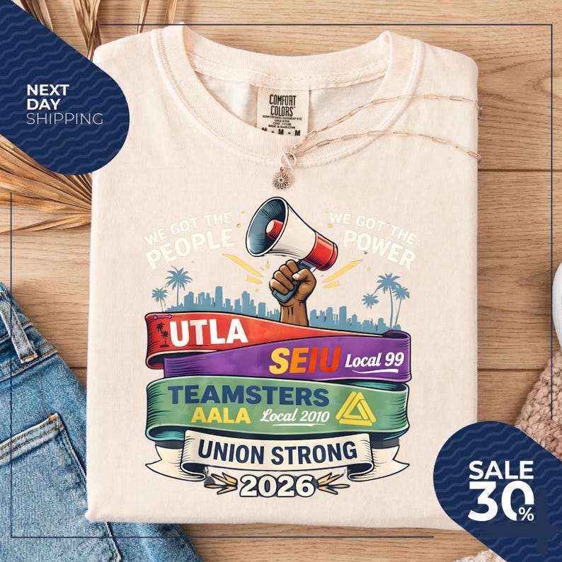 May include: Cream-colored t-shirt with a graphic featuring a megaphone, cityscape, and text including "We Got The People" and "Union Strong 2026." Ribbons display "UTLA," "SEIU," and "Teamsters." A sale of 30% is advertised.