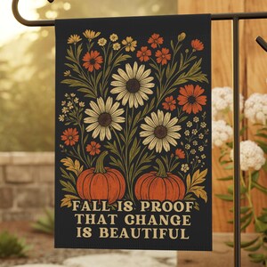 Puede incluir: Una bandera de jardín negra con un diseño floral y de calabazas. La bandera presenta calabazas naranjas, margaritas blancas y flores naranjas. El texto "FALL IS PROOF THAT CHANGE IS BEAUTIFUL" está impreso en la bandera.