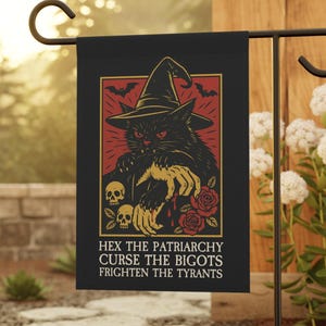 Può includere: Bandiera da giardino nera con un gatto nero con cappello da strega, con il testo "HEX THE PATRIARCHY CURSE THE BIGOTS FRIGHTEN THE TYRANTS". La bandiera ha un bordo rosso e oro, con teschi, rose e pipistrelli.