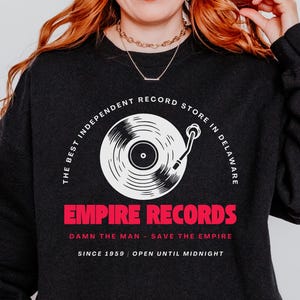 Puede incluir: Sudadera negra con un gráfico de tocadiscos blanco y el texto "The Best Independent Record Store in Delaware" y "Empire Records" en rojo. También se ve el texto "Damn the Man - Save the Empire" y "Since 1959 | Open Until Midnight".