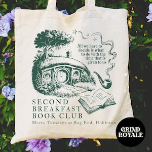 May include: Cream-colored tote bag with a green illustration of a hobbit hole, tree, and text. The text reads "SECOND BREAKFAST BOOK CLUB" and "All we have to decide is what to do with the time that is given to us."
