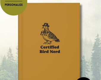 May include: Mustard-colored hardcover journal with a bird illustration wearing a hat and binoculars. The text "Certified Bird Nerd" is below the bird. The journal also says "Jack's Birding Journal" and "Hardcover Journal, Personalize".