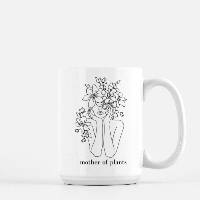 May include: White ceramic mug with a black line drawing of a woman with flowers in her hair. The text "mother of plants" is printed on the mug.