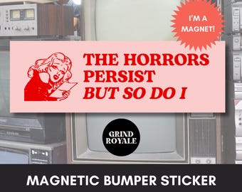 May include: A pink magnetic bumper sticker with the text "THE HORRORS PERSIST BUT SO DO I" in red. It features a red illustration of a woman and the words "I'M A MAGNET!" in a starburst. The Grind Royale logo is also visible.