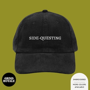 May include: Black corduroy baseball cap with the embroidered text "SIDE-QUESTING" in white. The cap features a curved brim and a structured crown. The Grind Royale logo is visible on the lower left.