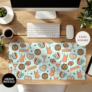 May include: A rectangular desk mat with a light blue background featuring a repeating pattern of orange swimsuits, disco balls, wine glasses, and the word "SHOWGIRL". The mat also includes the text "T.S." inside a heart.
