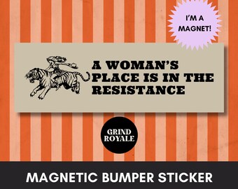 May include: A rectangular magnetic bumper sticker with the text "A Woman's Place Is In The Resistance" and a graphic of a woman riding a tiger. The sticker also has the text "I'M A MAGNET!" and "GRIND ROYALE".