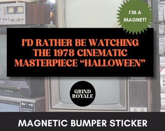 May include: A black magnetic bumper sticker with orange text that reads "I'D RATHER BE WATCHING THE 1978 CINEMATIC MASTERPIECE 'HALLOWEEN'". A green starburst magnet is above the text. The Grind Royale logo is also visible.
