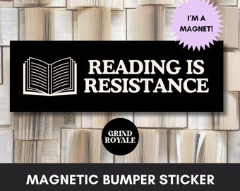 May include: A rectangular black magnetic bumper sticker featuring a white open book icon and the text READING IS RESISTANCE in bold white capital letters. A light purple starburst shape contains the text I'M A MAGNET! and a black circle says GRIND ROYALE.