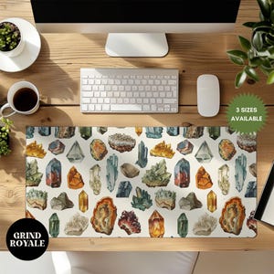 Puede incluir: Una alfombrilla de escritorio blanca con un patrón colorido de varias piedras preciosas. La alfombrilla presenta una variedad de formas y colores, incluyendo rojo, azul, verde y amarillo. El texto "Grind Royale" está impreso en la esquina inferior izquierda.