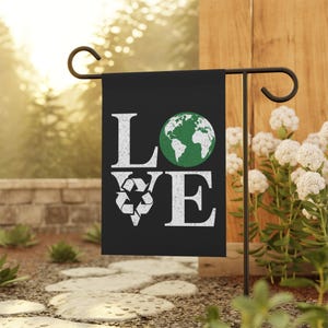 Może przedstawiać: Czarna flaga ogrodowa z napisem "LOVE" białymi literami. Litera "O" została zastąpiona zielonym globusem, a litera "V" białym symbolem recyklingu.