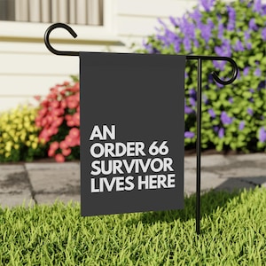 Peut inclure: Un drapeau de jardin noir avec du texte blanc qui dit "An Order 66 Survivor Lives Here". Le drapeau est affiché sur un support de drapeau de jardin en métal noir.