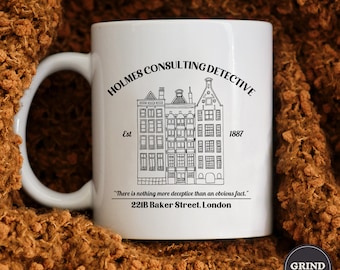 Op de afbeelding: Witte keramische mok met een zwart-witte illustratie van een gebouw met de tekst "Holmes Consulting Detective Est 1887" en het citaat "Er is niets misleidend dan een voor de hand liggend feit." 221B Baker Street. Londen.