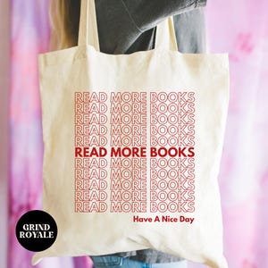 May include: A white canvas tote bag with the text "READ MORE BOOKS" repeated in red, stacked vertically. The text "Have A Nice Day" is printed below the repeated text. The text "GRIND ROYALE" is printed in the bottom left corner.