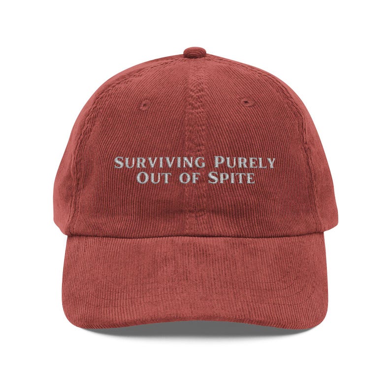 May include: A red corduroy baseball cap with the text "SURVIVING PURELY OUT OF SPITE" embroidered in white.