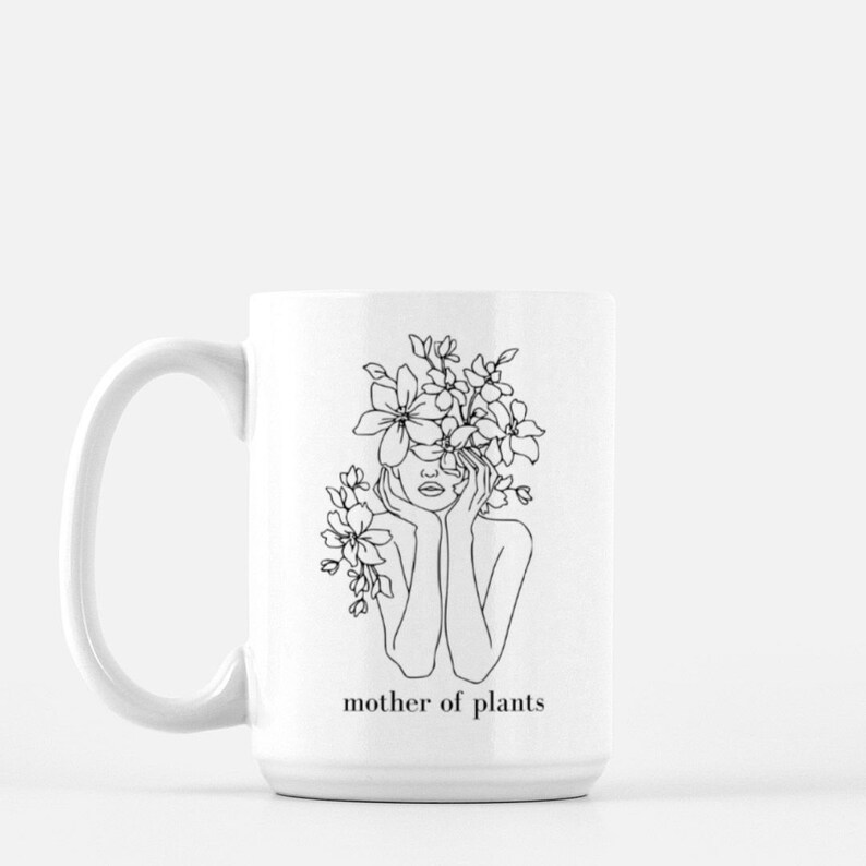 May include: White ceramic mug with a black line drawing of a woman with flowers covering her head. The text "mother of plants" is printed below the image.