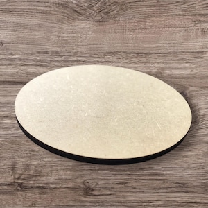 Puede incluir: Un posavasos ovalado de madera con una superficie beige claro y un borde negro. El posavasos está hecho de un material de madera de color claro y está diseñado para proteger las superficies de la condensación de las bebidas.