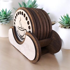 Puede incluir: Un juego de posavasos de madera y soporte. Los posavasos redondos son de color marrón oscuro, con un diseño de taza de café en uno. El soporte es de color marrón claro con un borde marrón oscuro. Los posavasos tienen unos 10 cm de diámetro.