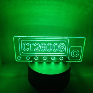May include: A green LED light with a clear acrylic panel displaying the text "CT26008". The light is on a black base.