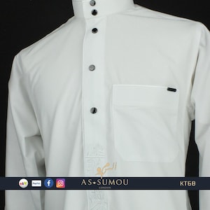 May include: White long-sleeve shirt with a button-up collar and a pocket on the left side. The shirt has a decorative pattern on the front and the text "AS-SUMOU LONDON" at the bottom.