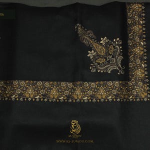 Può includere: Uno scialle nero con un intricato bordo floreale dorato e marrone e un motivo paisley abbinato nell'angolo. Il tessuto include il testo STYLE: ASU706, il logo AS-SUMOU, l'URL del sito web e icone per morbidezza al tatto e traspirabilità.