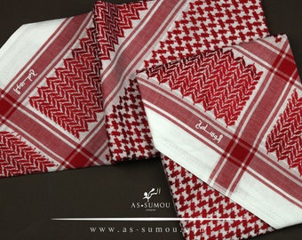 May include: Several red and white keffiyeh scarves are displayed, showcasing a traditional Middle Eastern design. The scarves feature a repeating pattern of red and white geometric shapes and stripes. The brand name and website are visible.