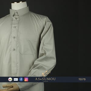 May include: A light gray long-sleeved shirt with a button-up collar and a single pocket on the left chest. The shirt has a traditional design with a button placket and a rounded hem. The shirt is made of a smooth, wrinkle-resistant fabric.