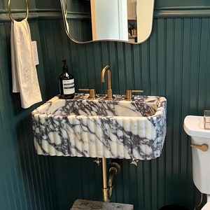 May include: A small bathroom with green wainscoting, a white toilet, and a marble sink with gold fixtures. The floor is tiled with hexagonal tiles.